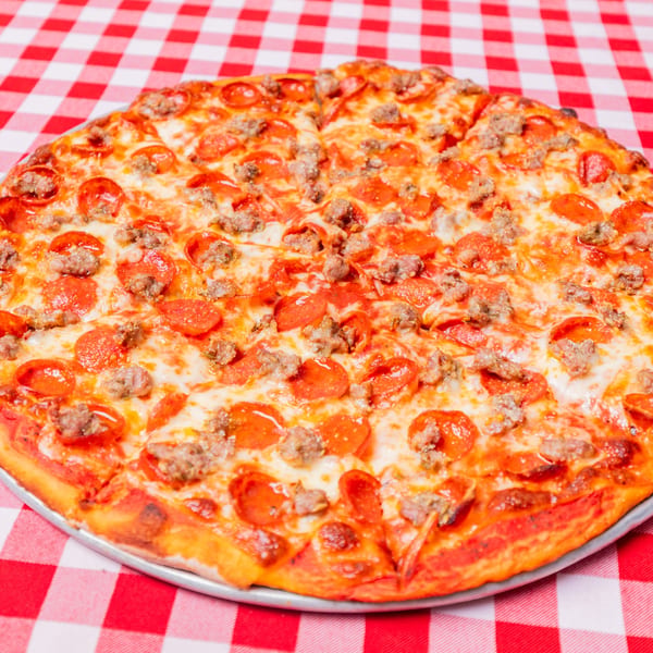 A whole Pietras Pizzeria pepperoni and sausage pizza on a red and white checkered tablecloth.