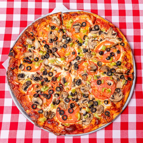 Pietras Pizzeria's whole veggie pizza with tomatoes, olives, mushrooms, and peppers on a red and white checkered tablecloth.