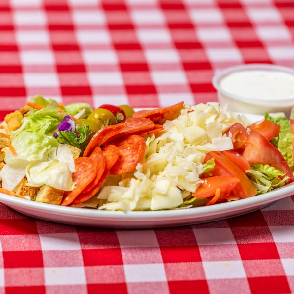 Pietras Pizzeria's large Italian salad with pepperoni, cheese, tomatoes, and olives on a checkered tablecloth.