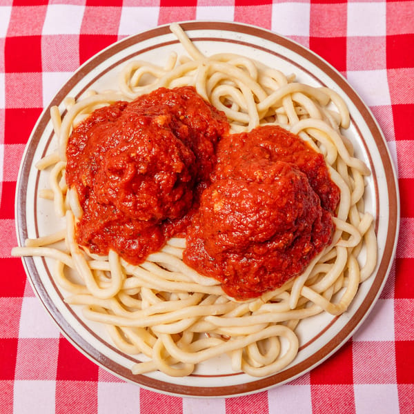 Plate of thick spaghetti with two large dollops of red marinara sauce on a red and white checkered tablecloth.