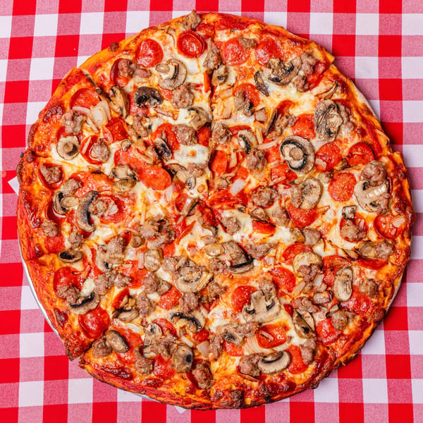 A whole Pietras Pizzeria pizza with pepperoni, sausage, mushrooms, and onions on a red and white checkered tablecloth.