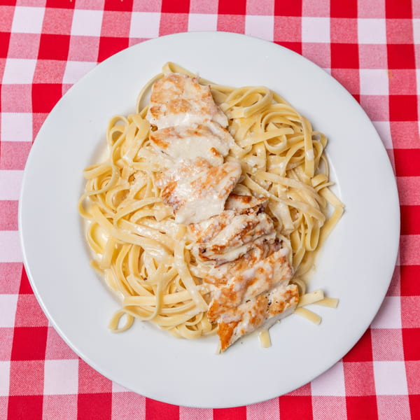 Chicken Alfredo pasta dish on a white plate, served on a red and white checkered tablecloth.